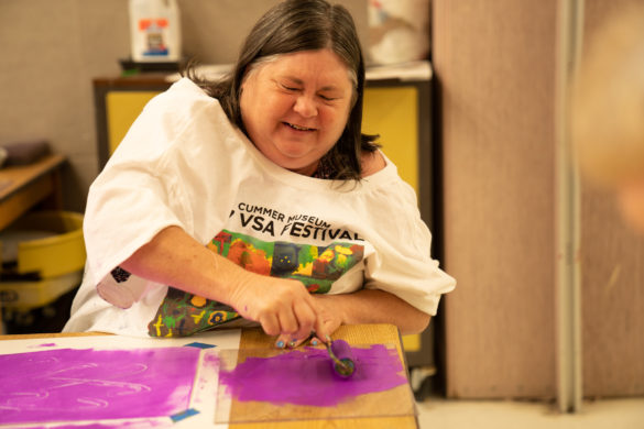 Woman with low vision creating a work of art depicting a flower with bright purple printmaking ink.